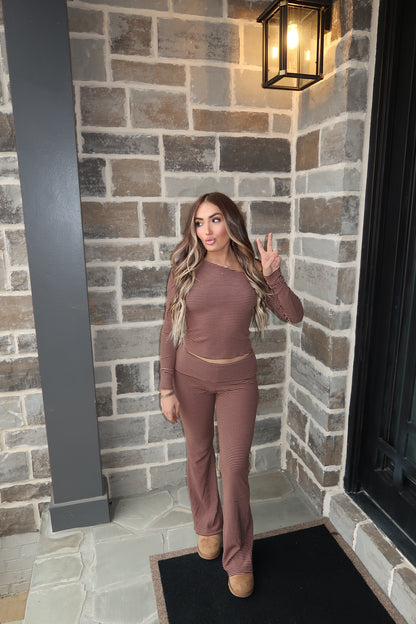 Woman in a brown outfit standing in front of a brick wall with a light fixture.