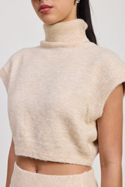 A close-up of a model wearing a soft, fuzzy cropped knit turtleneck sweater in a light cream or oatmeal color.
